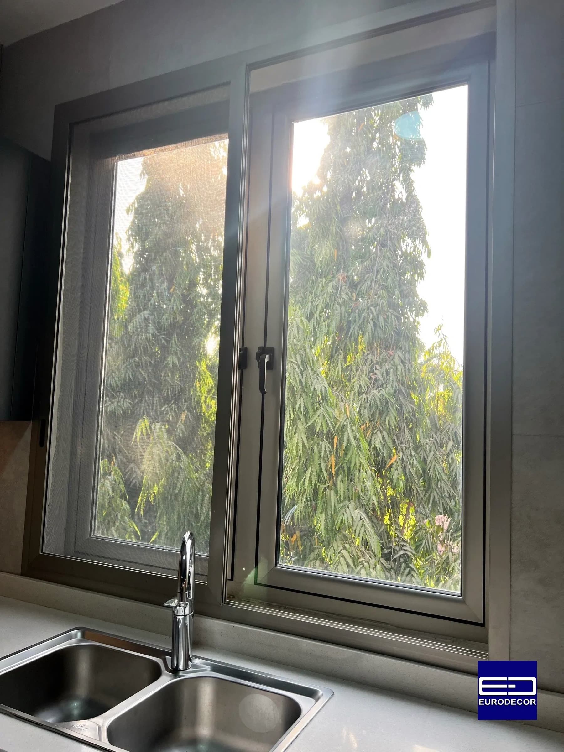 An aluminium window with a net screen, over a kitchen sink