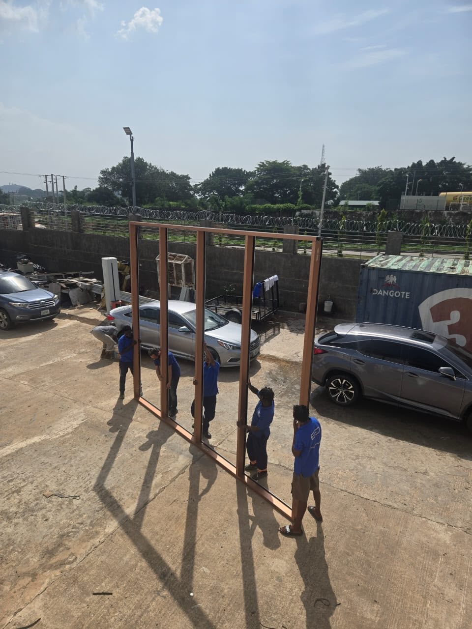The Euro Decor crew in blue carrying a large bronze aluminium frame across the yard
